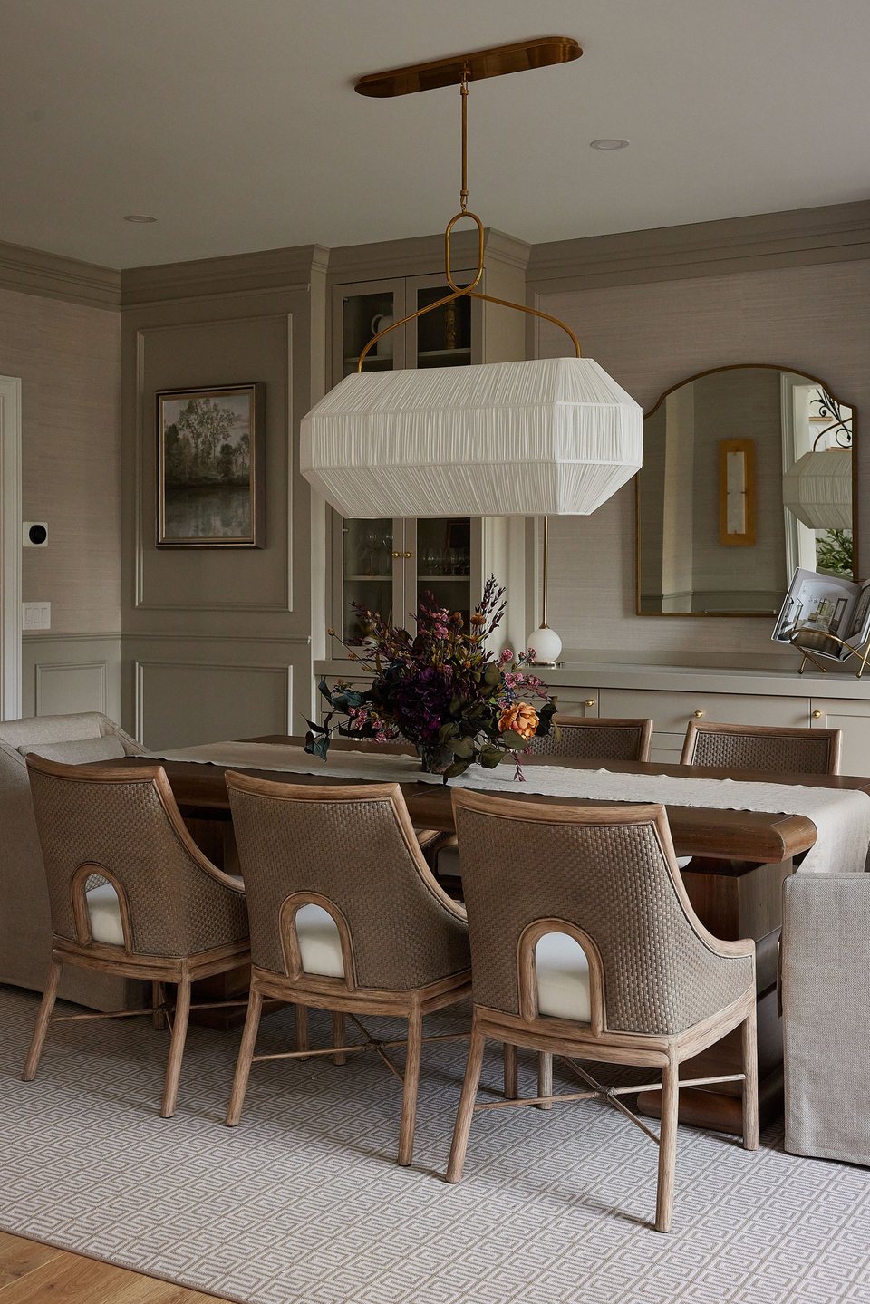 A softly lit dining room designed by UA Design Group, with woven chairs and a sculptural pendant light